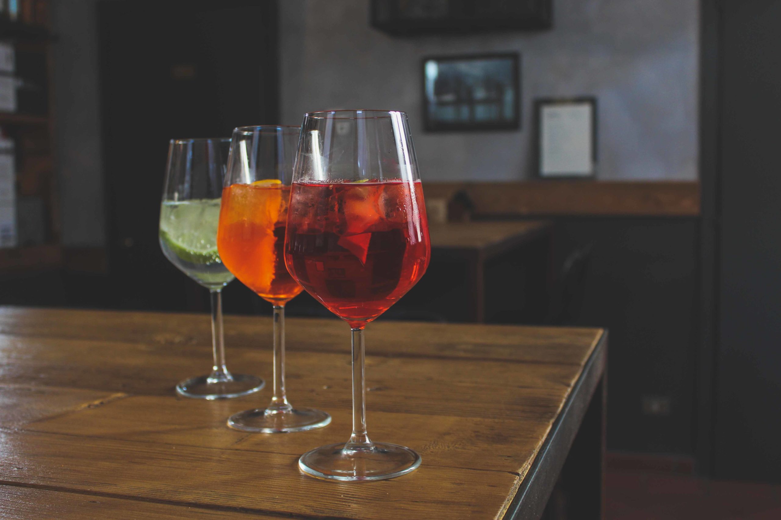 tre bicchieri con aperitivo in fila su un tavolo di legno